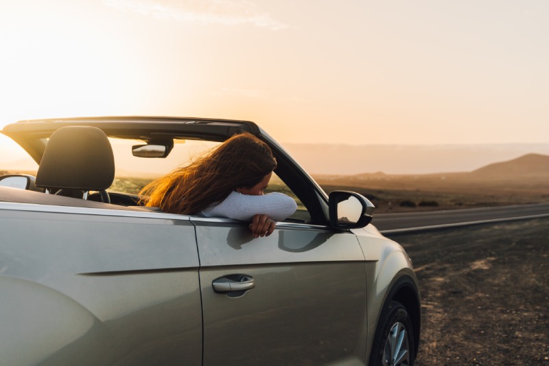 A woman taking in the view from a TopCar convertible at sunset.